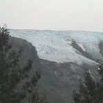 A view of the top of a mountain with trees in front.