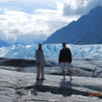 Two men standing on a rock surface in front of a glacier.